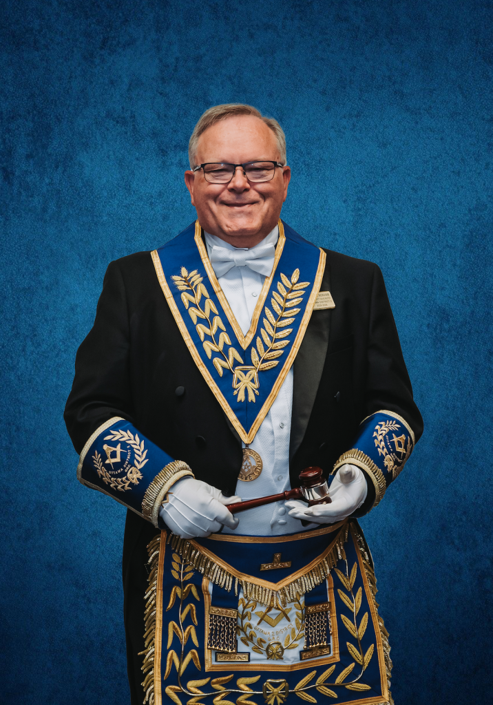 Formal portrait of the District Deputy Grand Master of Ottawa District 2 wearing ornate Masonic regalia against a blue textured backdrop, representing leadership within the Grand Lodge of Ontario.